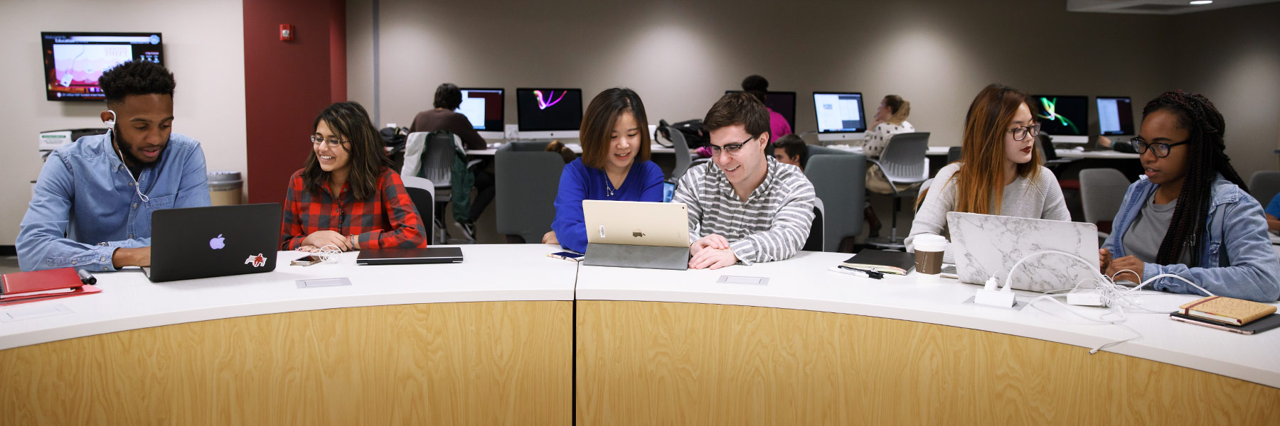 Three groups of two students discuss what they're looking at on a laptop.