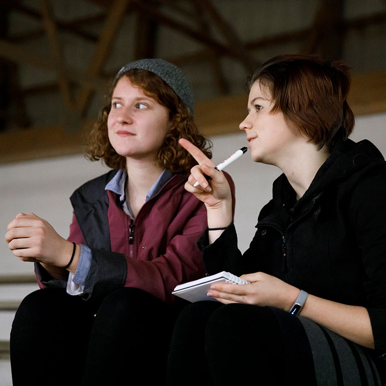 Two students watch something off camera.